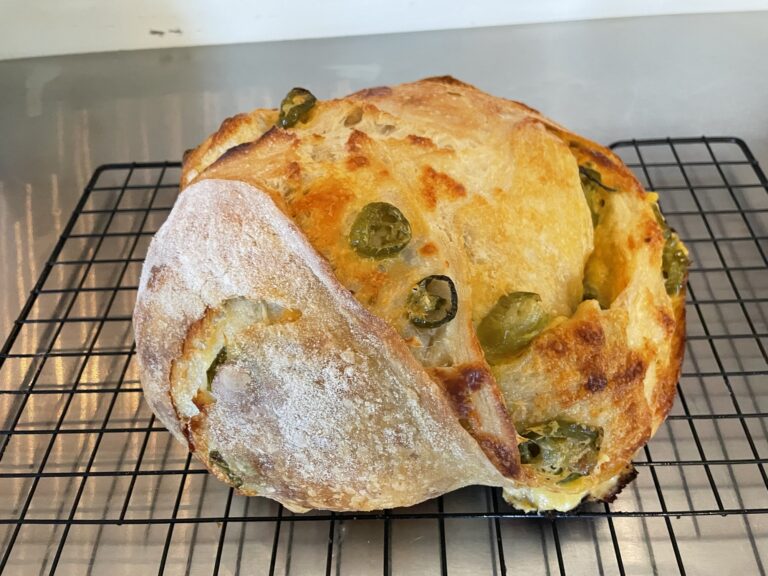 A beautifully scored loaf of cheesy jalapeño sourdough reveals melted cheese and spicy jalapeños inside.