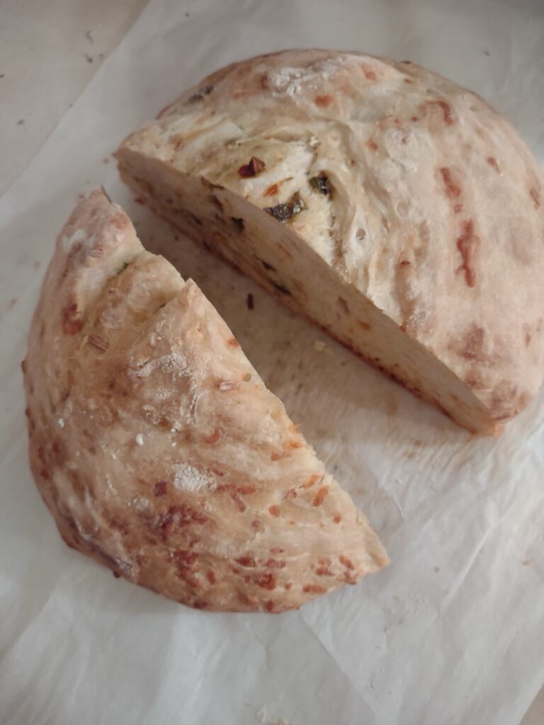 A halved loaf of cheesy jalapeño bread, baked without a Dutch oven, showing the softer, light-colored crust and melted cheese inside.