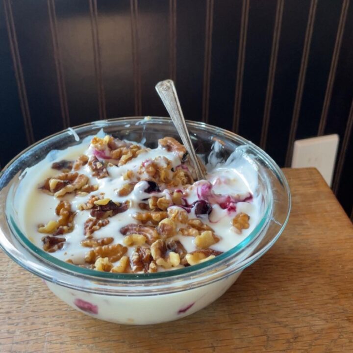 The successful result of the recipe: a glass bowl of thick, gelatin-free yogurt garnished with walnuts and frozen berries.