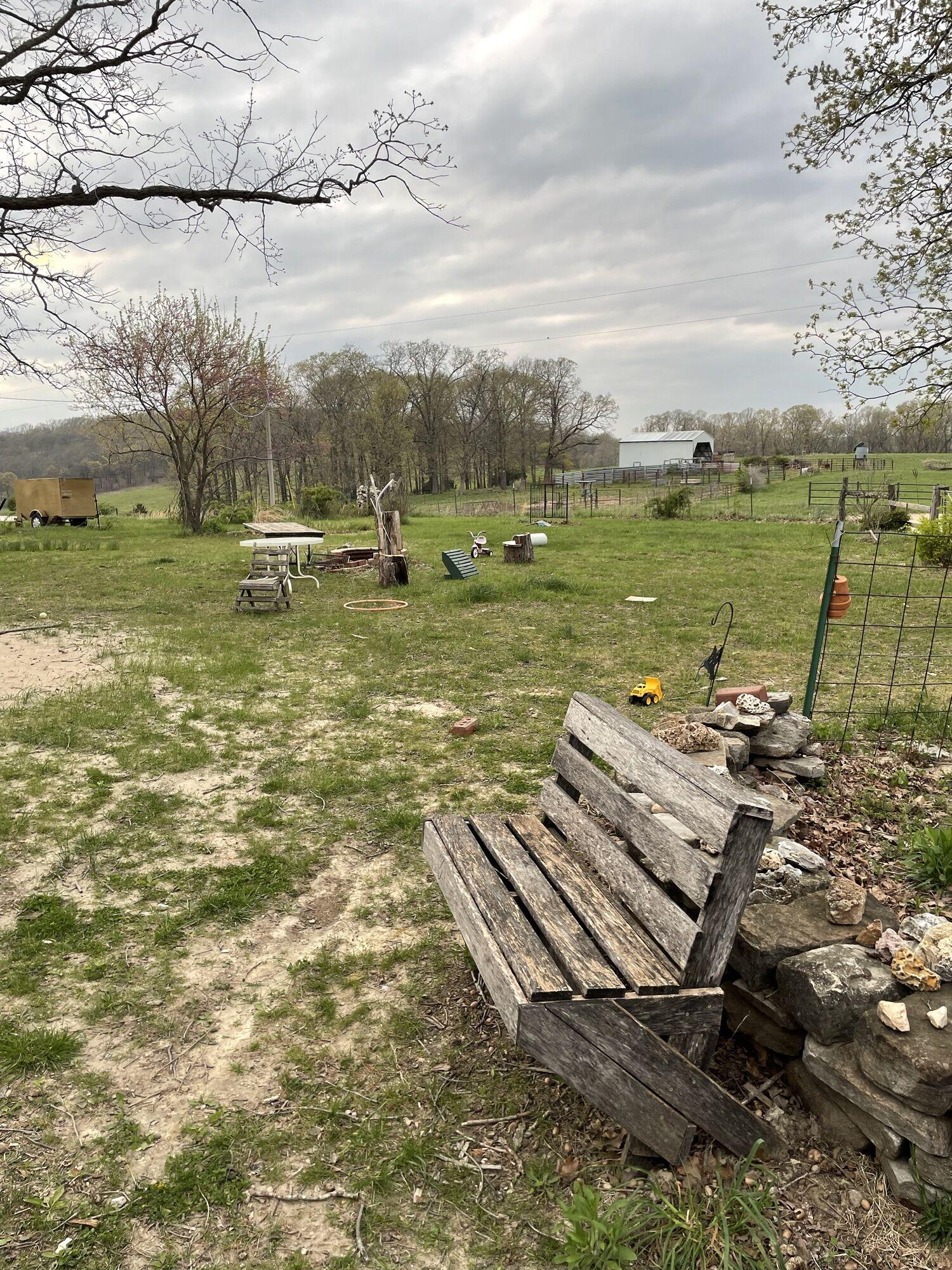 An early spring scene with small leaves on the trees and patches of green grass. An empty bench in the foreground awaits warmer weather.