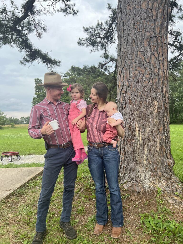 A Smith family photo where we look at each other and smile, all wearing shades of the blog's main color, pink: Carson, my husband, is in a salmon-colored western shirt; I'm in a dusty rose pink western shirt; our daughter Timberlynn is in bright pink Carhartt overalls and rain boots; and our baby, Wrangler, is in pink pants.
