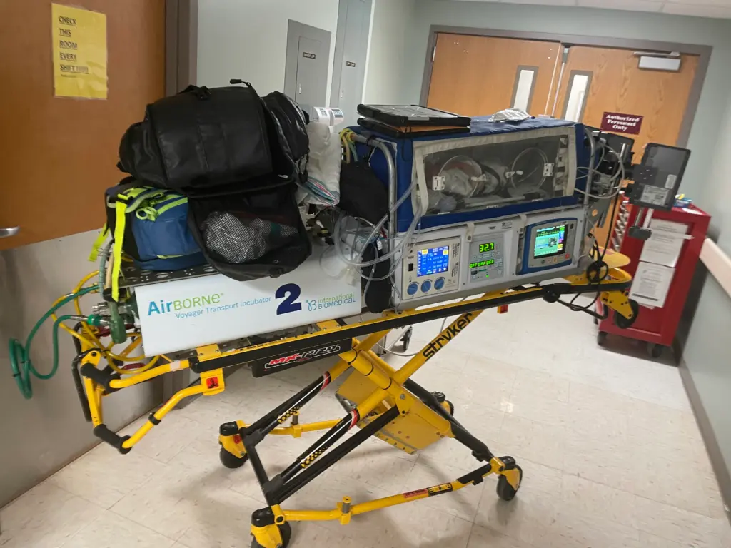 Too Late for the Hospital: My 37-Week Unplanned Home Birth and the Helicopter Ride to the NICU 9 A full view of the transport incubator stretcher, fully loaded, locked, and ready for transport. Baby Wrangler is inside, and the monitor screens below the unit are fully lit, displaying her vital signs and heart rhythm.