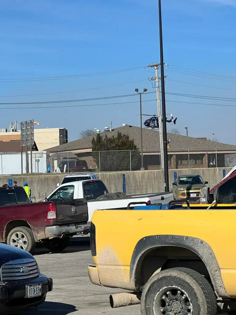 Too Late for the Hospital: My 37-Week Unplanned Home Birth and the Helicopter Ride to the NICU 10 A medical transport helicopter lifts off a ground pad into a clear blue sky, transporting newborn Wrangler to the NICU. A parking lot and a building are in the foreground.