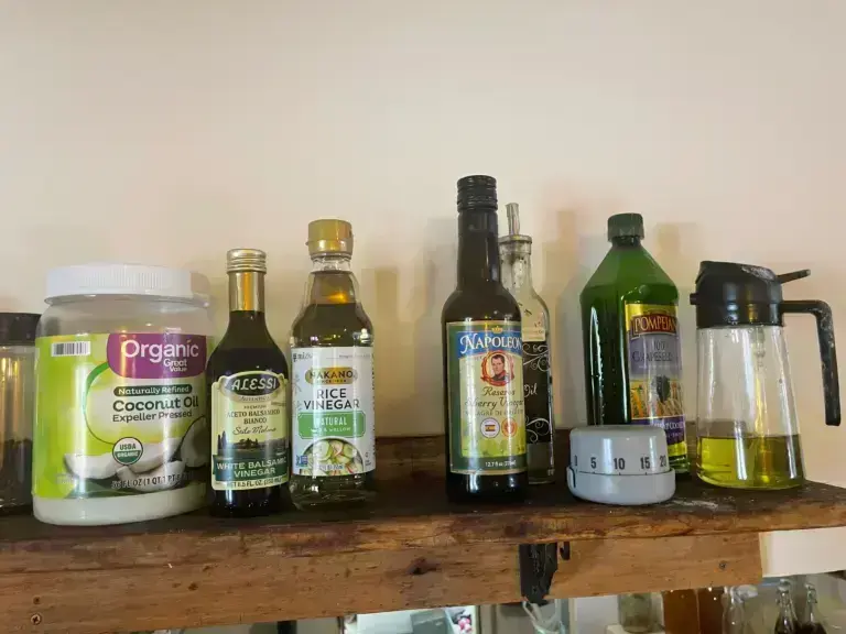 A collection of vinegars, oils, and a kitchen timer on a wooden shelf, representing the tools used to balance flavors in cooking.