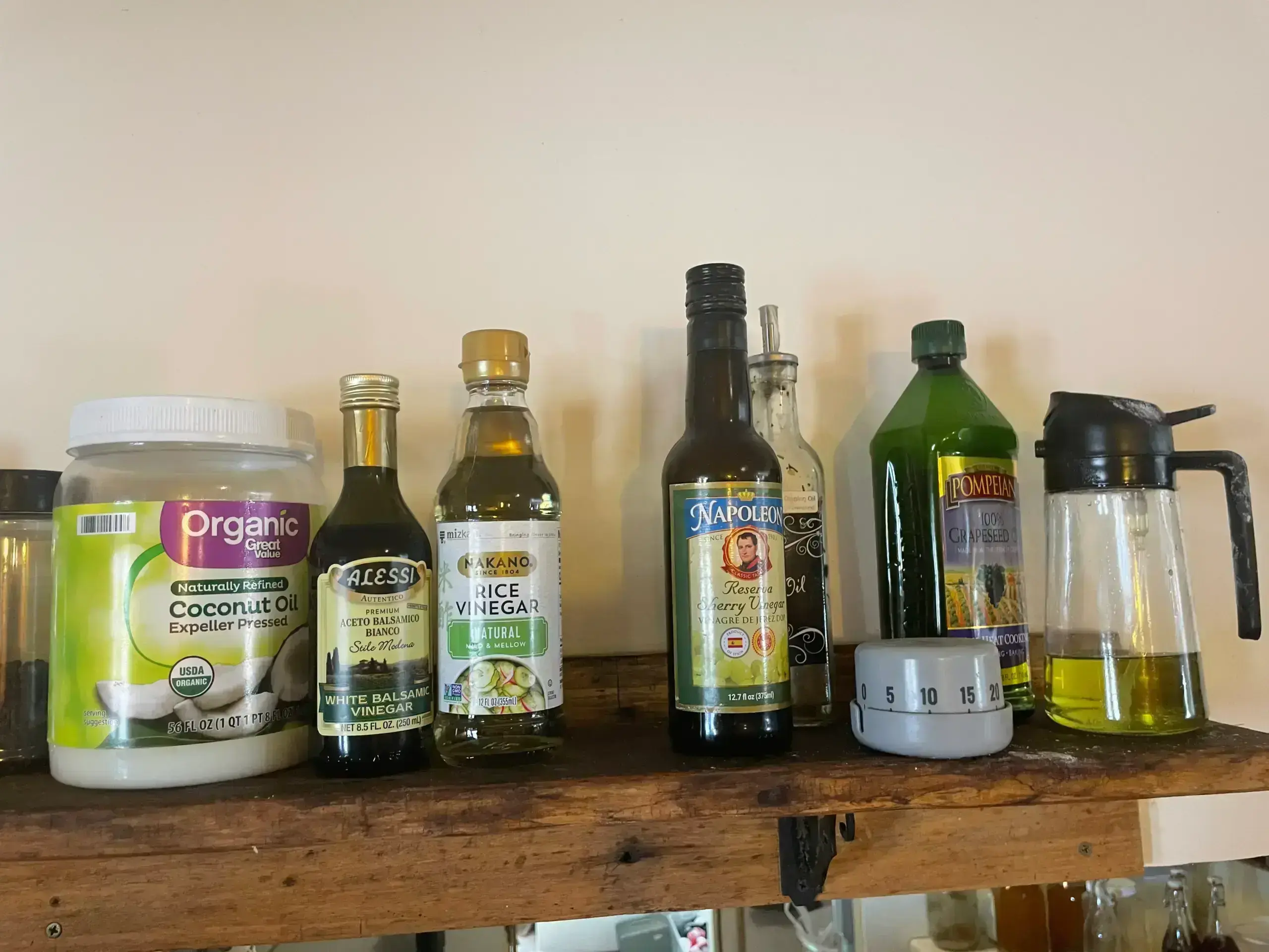 A collection of vinegars, oils, and a kitchen timer on a wooden shelf, representing the tools used to balance flavors in cooking.