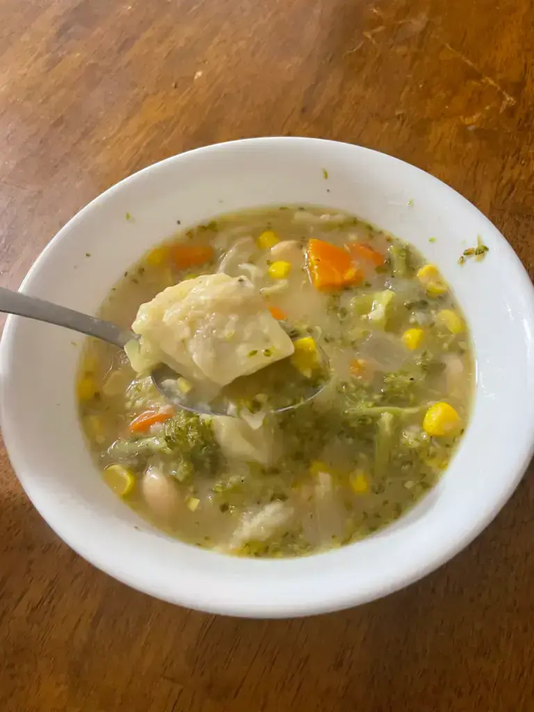 Rosemary garlic dumpling on a spoon over a bowl of steamy hot plant based soup.
