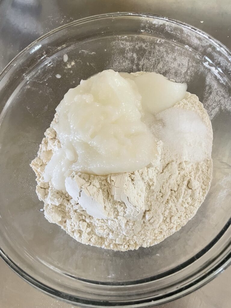 Semi-solid and scoopable coconut oil sits atop dry ingredients for making flaky vegan sourdough biscuits.