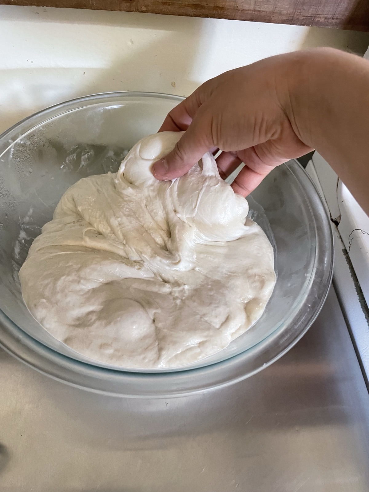 A hand stretching bubbly, elastic sourdough dough from a bowl, showing how to fit sourdough into a busy schedule by reading dough bubbles.