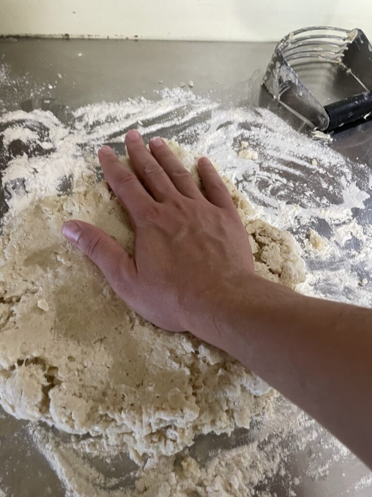 Hand pressing down to compress the layers of folded dough in a simple lamination process.