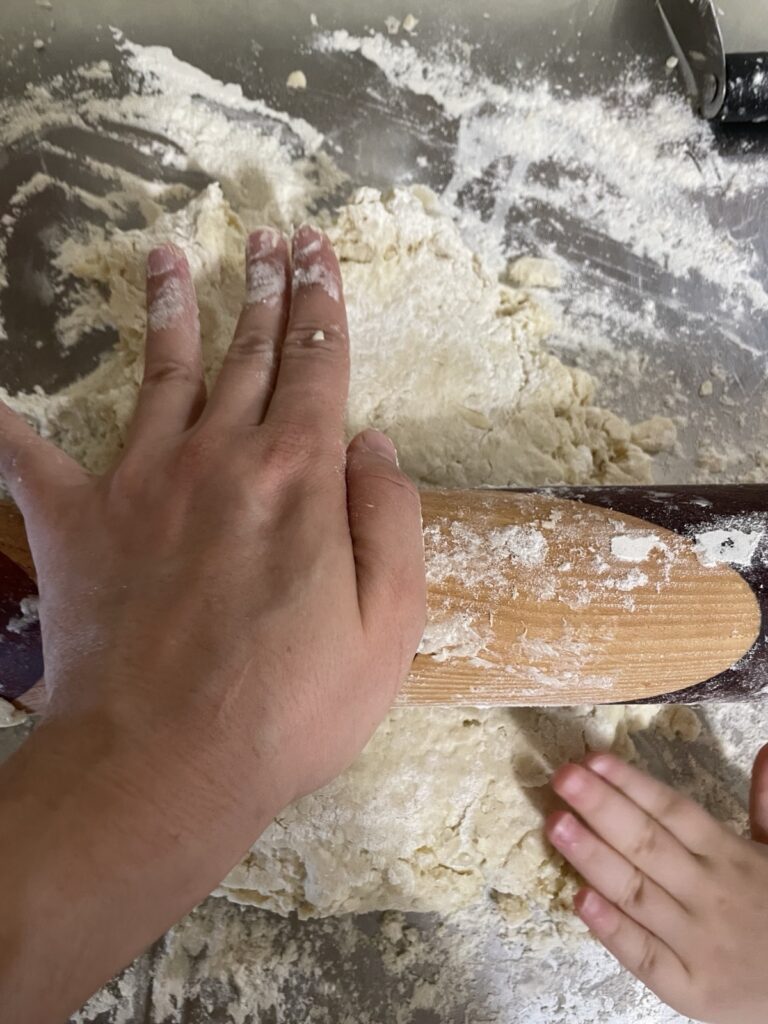Pressing down on a rolling pin to compress folded dough in a simple lamination process.