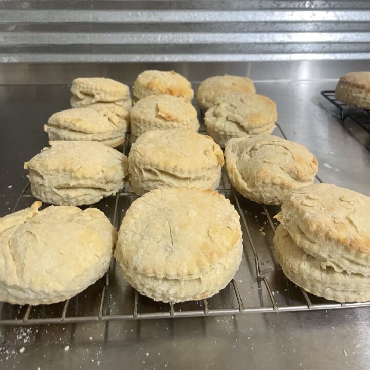 Flaky golden brown sourdough biscuits on cooling racks, demonstrating how to make flaky sourdough biscuits using both butter (left) and vegan coconut oil (right).