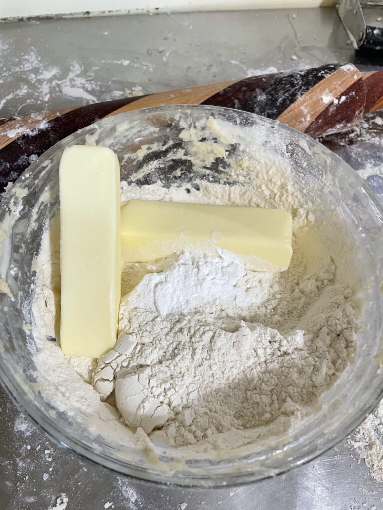 Two sticks of butter sit atop the dry ingredients for making sourdough biscuits.